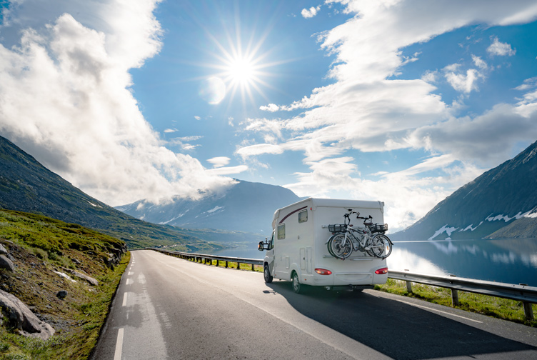 RV driving on a mountain road in the sun.